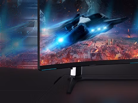On the monitor display which is pivoted to the right, a rocket ship is flying over a city landscape at night time, with light emitting from the rear engine exhausts.